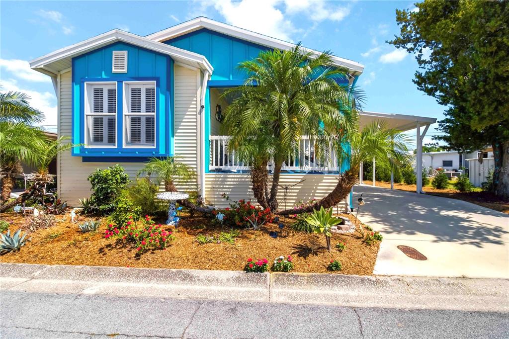 A bright blue and beige manufactured home features a front porch, palm trees, and carport — 915 50TH AVENUE W, BRADENTON, FL
