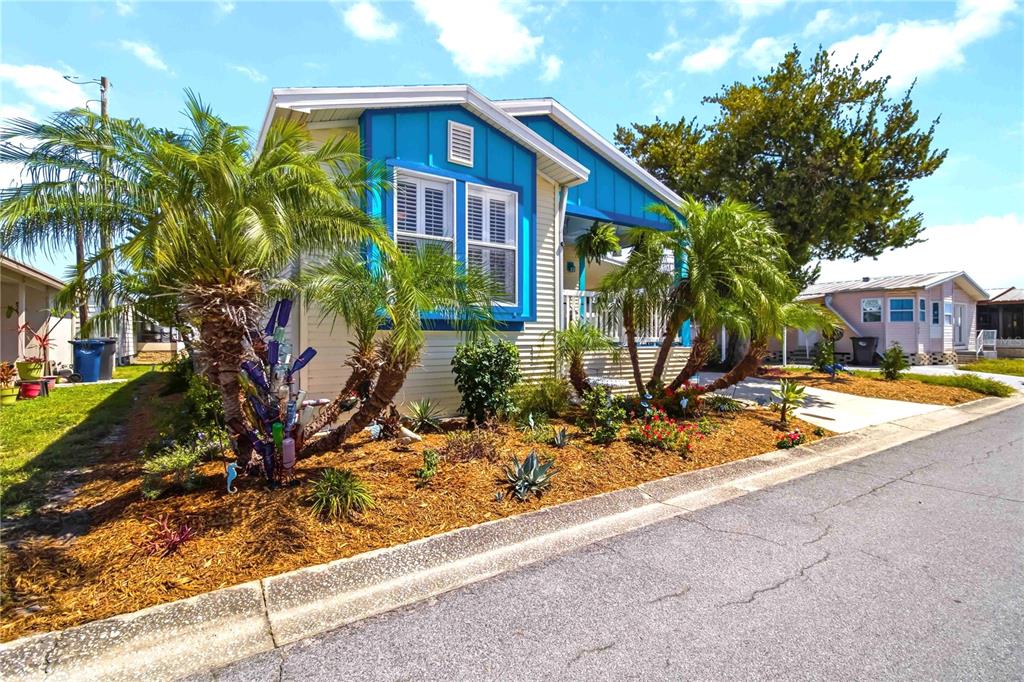 A covered porch features blue flooring, two chairs, a small table, and beach-themed decor — 915 50TH AVENUE W, BRADENTON, FL
