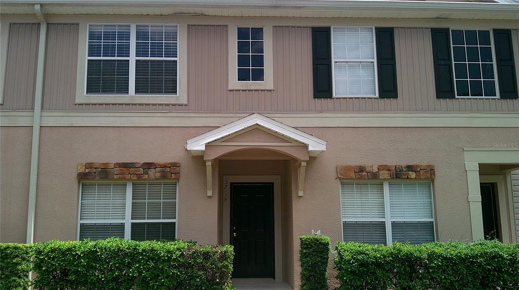 A two-story townhouse exterior features a covered entryway, stone accents, and a green hedge — 5718 FISHHAWK RIDGE DRIVE, LITHIA, FL