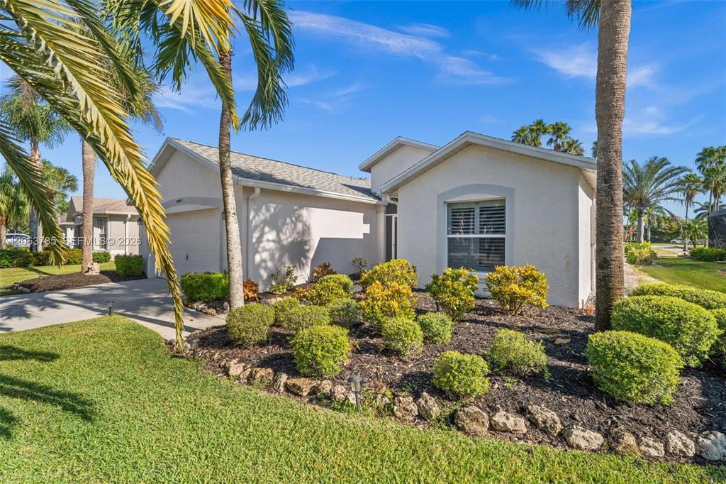A single-story house with a beige stucco exterior, a two-car garage, and landscaped front yard — 21489 SHERIDAN RUN, ESTERO, FL