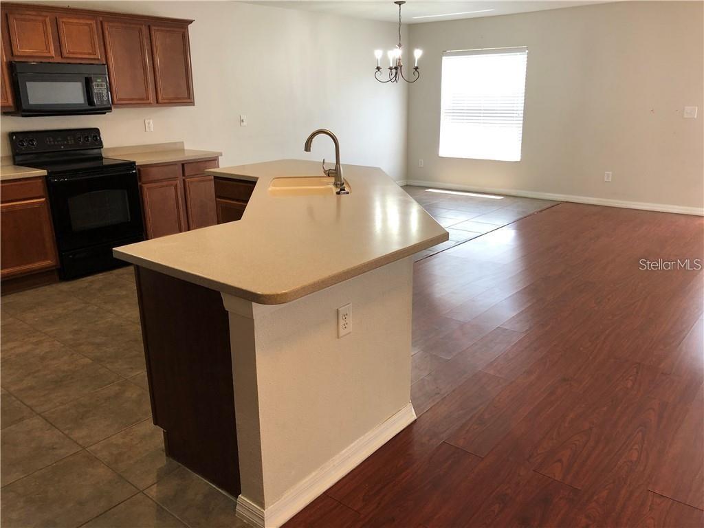 A kitchen with a central island, wood cabinets, black appliances, and wood-look flooring — 5116 CELLO WOOD LANE, WESLEY CHAPEL, FL