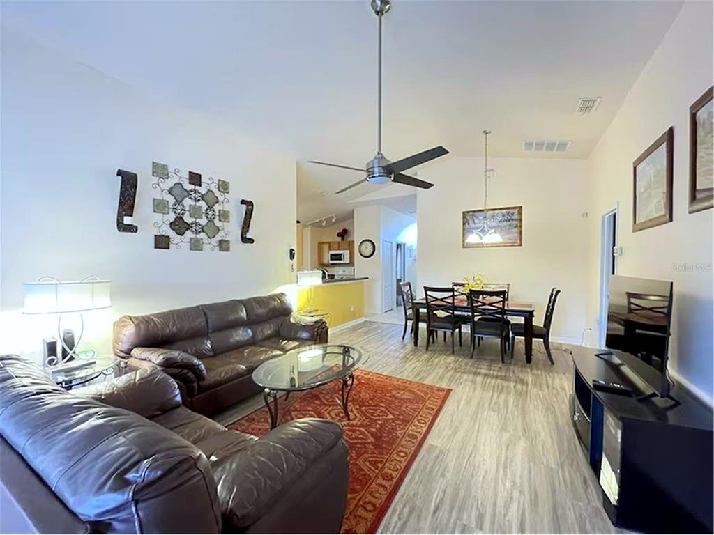 A living room with a brown leather sofa, dining area, and light wood-look flooring — 136 STARBIRD COURT, DAVENPORT, FL
