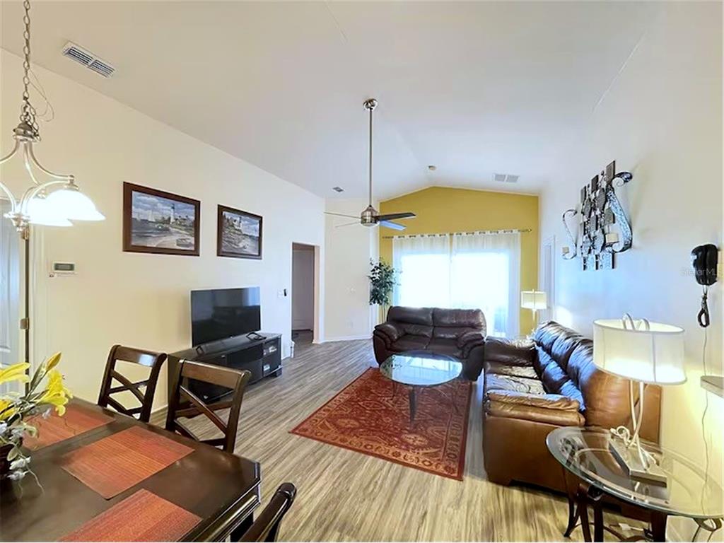 A living room and dining area feature wood-look flooring, vaulted ceilings, and a ceiling fan — 136 STARBIRD COURT, DAVENPORT, FL