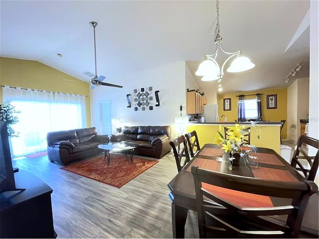 An open-concept living and dining area features wood-look flooring, a ceiling fan, and yellow walls — 136 STARBIRD COURT, DAVENPORT, FL