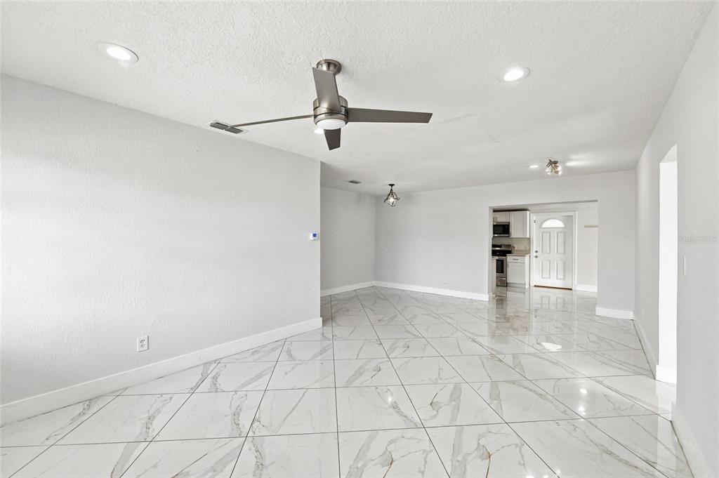 A bright, open-concept living area features white marble-look tile flooring and a ceiling fan — 7805 WINSTON LANE, TAMPA, FL