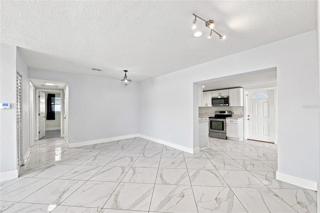 A dining area with white marble-patterned tile floors opens into a kitchen with white cabinets — 7805 WINSTON LANE, TAMPA, FL