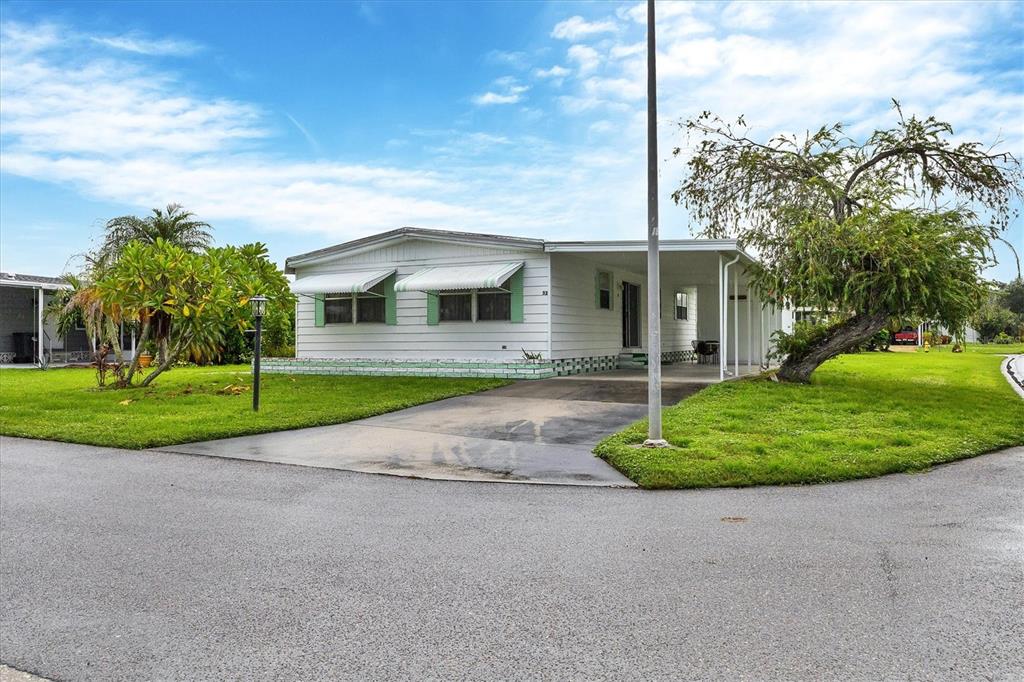 A single-story mobile home with white siding, green trim, and a carport sits on a lawn — 6710 36TH AVENUE E UNIT 52, PALMETTO, FL