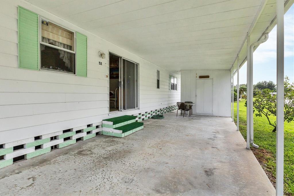 A covered concrete patio features a sliding glass door, green steps, and a storage closet — 6710 36TH AVENUE E UNIT 52, PALMETTO, FL
