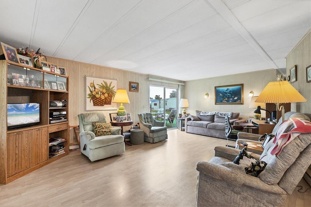 A living room features wood-paneled walls, light-colored flooring, multiple armchairs, a sofa, and sliding glass doors — 6710 36TH AVENUE E UNIT 52, PALMETTO, FL