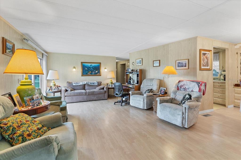 A living room with light wood-paneled walls, light wood flooring, and several pieces of furniture — 6710 36TH AVENUE E UNIT 52, PALMETTO, FL
