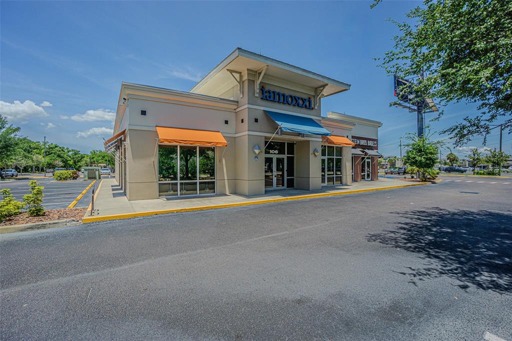 A commercial building with a tan exterior, orange and blue awnings, and a parking lot — 5395 E BAY DRIVE, CLEARWATER, FL