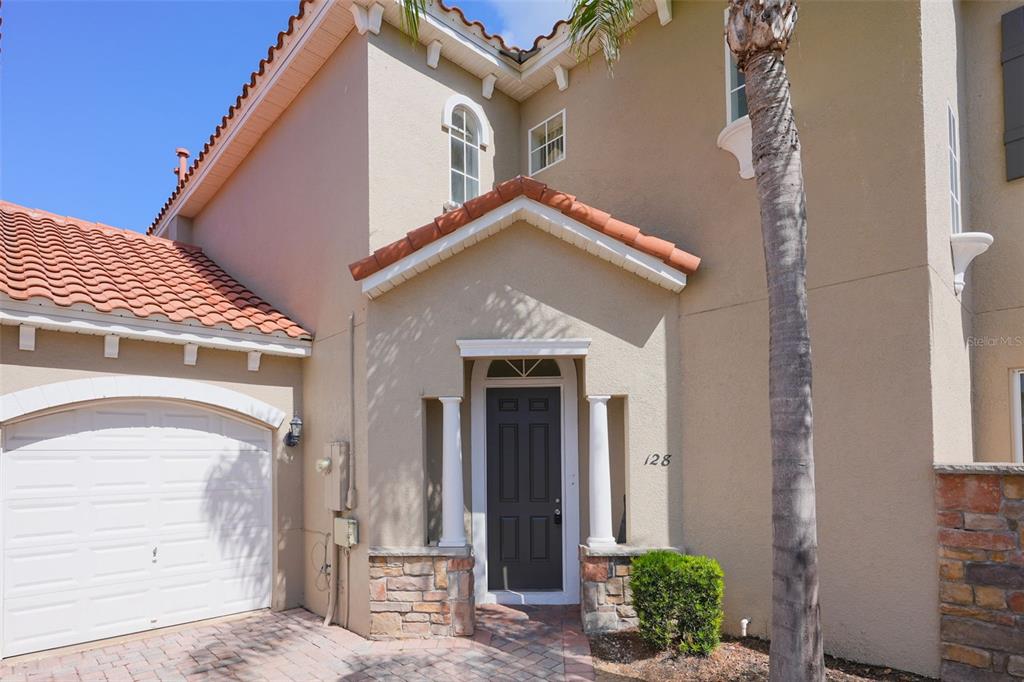 A tan stucco house exterior features a tiled roof, a garage, and a front entryway — 128 BRUNELLO DRIVE, DAVENPORT, FL