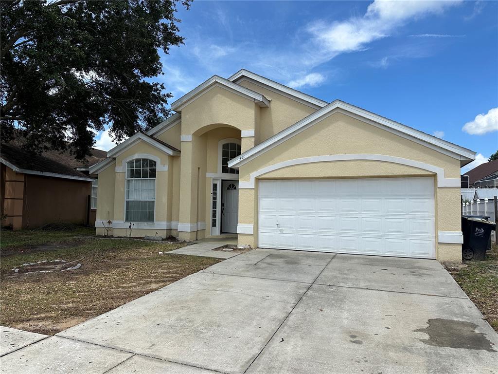 A single-story house with a yellow stucco exterior, white trim, and a two-car garage — 311 DOWNING CIRCLE, DAVENPORT, FL