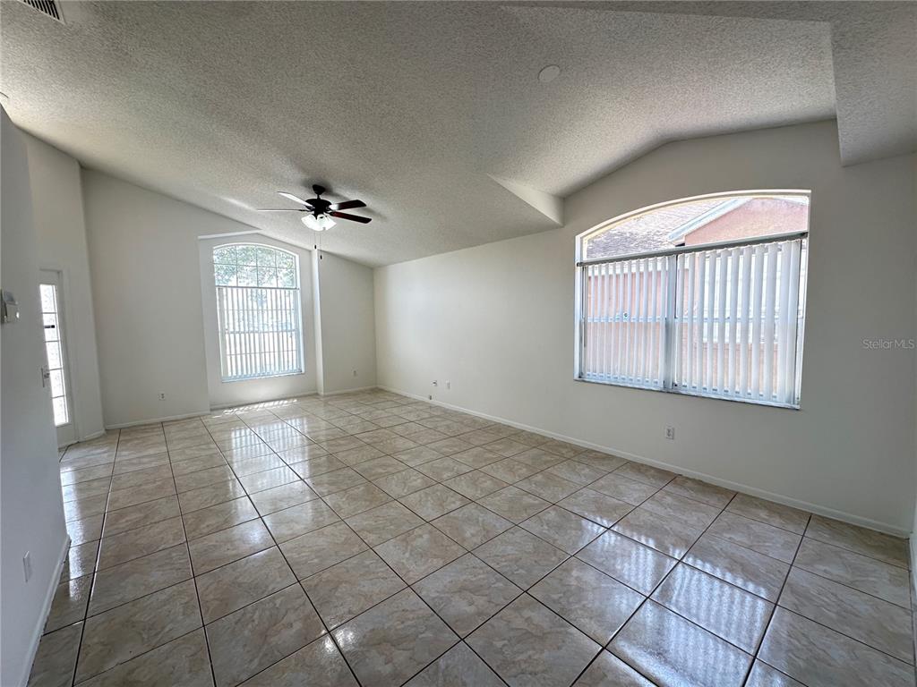 A spacious living room features vaulted ceilings, tile flooring, and two large arched windows — 311 DOWNING CIRCLE, DAVENPORT, FL