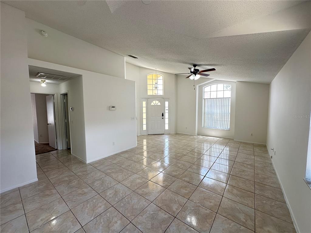 A bright, open-concept living area features high ceilings, tile flooring, and a front entryway — 311 DOWNING CIRCLE, DAVENPORT, FL