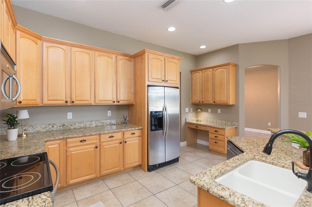 A kitchen features light wood cabinets, granite countertops, stainless steel appliances, and a built-in desk — 11544 PINE HOLLOW WAY, DADE CITY, FL