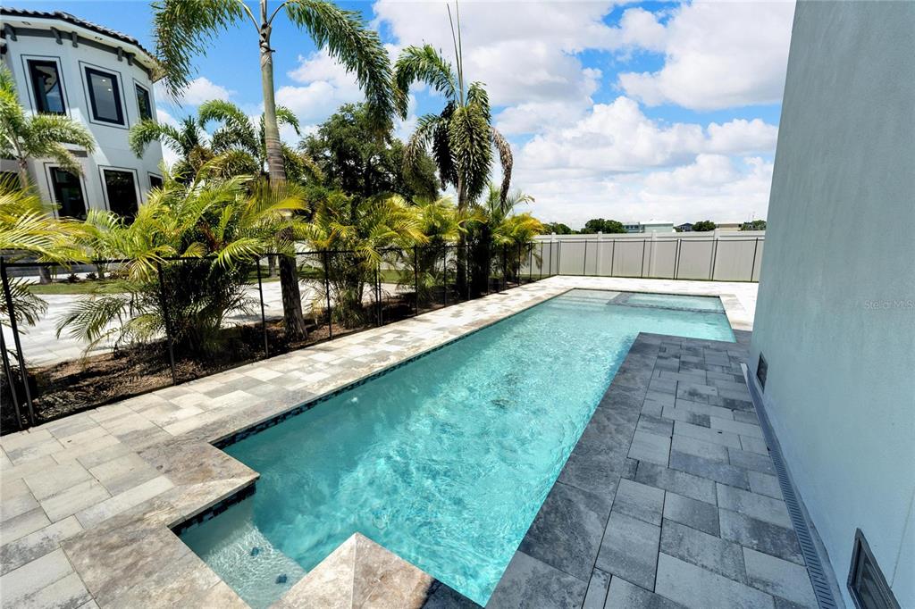 A rectangular swimming pool with a spa sits on a stone patio beside a house — 517 TREVISO DRIVE, APOLLO BEACH, FL