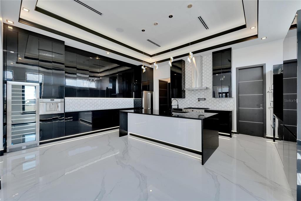 A modern kitchen features high-gloss black cabinetry, a white marble island, and white marble flooring — 517 TREVISO DRIVE, APOLLO BEACH, FL