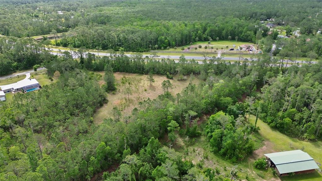 An aerial view shows a cleared, grassy lot surrounded by dense trees and nearby houses — 0 W SR 40 HIGHWAY, ORMOND BEACH, FL
