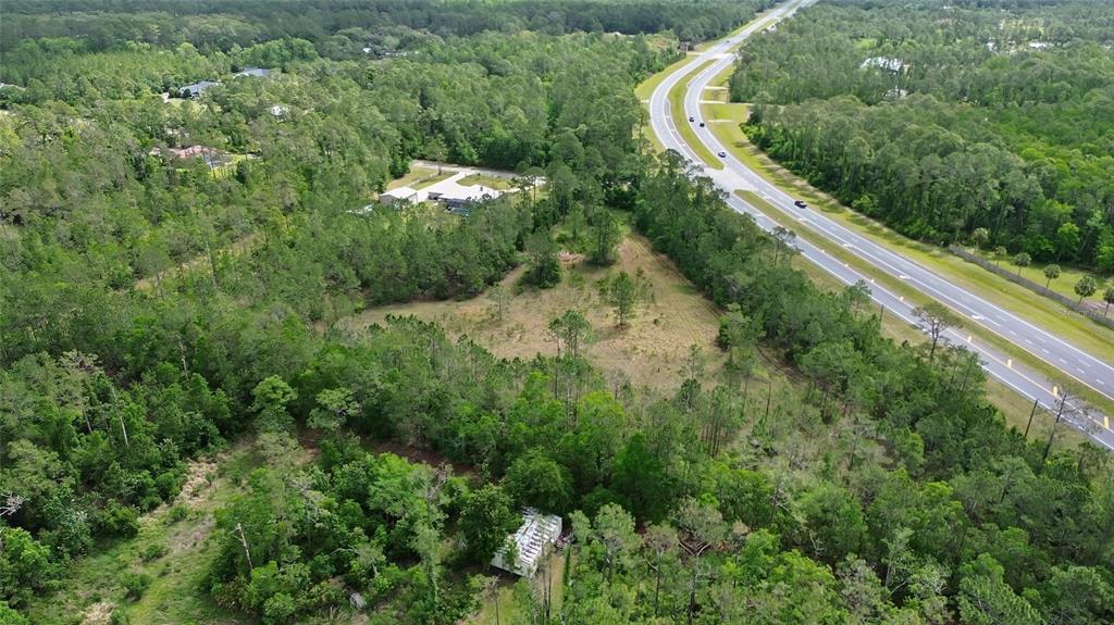 An aerial view shows a wooded lot adjacent to a divided highway with a small structure — 0 W SR 40 HIGHWAY, ORMOND BEACH, FL