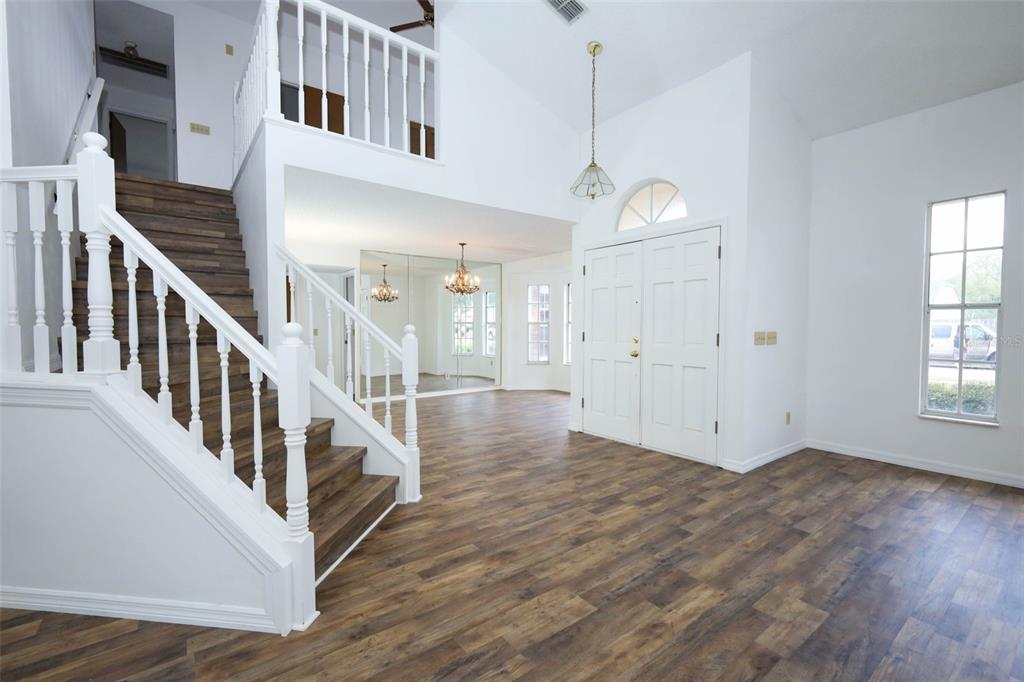 An entryway features wood-look flooring, a white staircase, a vaulted ceiling, and double front doors — 1675 THORNHILL CIRCLE, OVIEDO, FL