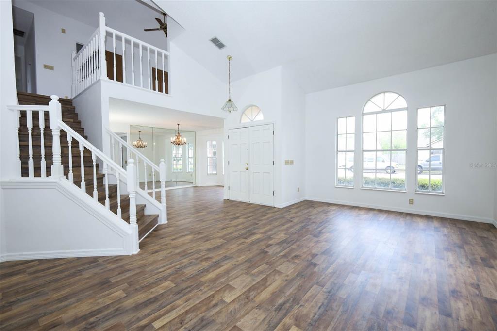 A bright living room features wood-look flooring, a staircase with white railings, and arched windows — 1675 THORNHILL CIRCLE, OVIEDO, FL