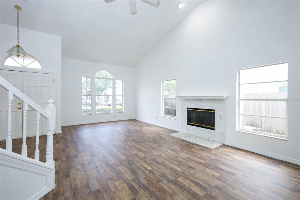 A living room features vaulted ceilings, wood-look flooring, a marble fireplace, and large windows — 1675 THORNHILL CIRCLE, OVIEDO, FL