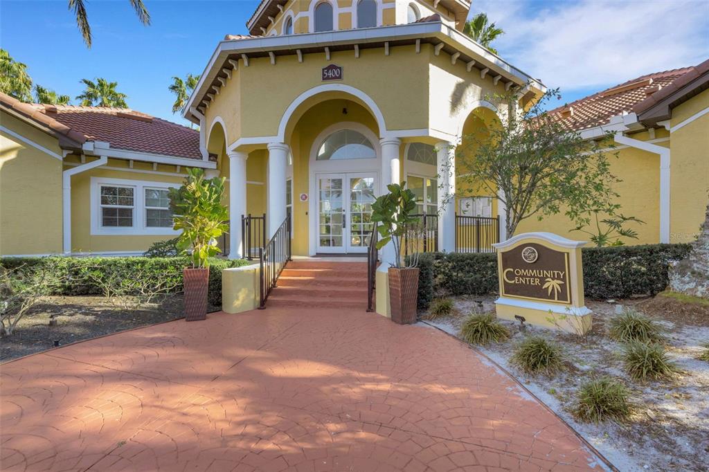 The exterior of a yellow community center building features a paved walkway and double doors — 5601 BENTGRASS DRIVE UNIT 10-202, SARASOTA, FL