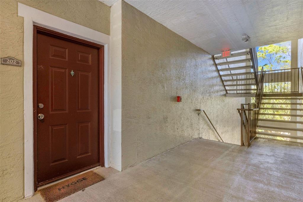 A brown apartment door labeled 202 sits next to an outdoor staircase and concrete landing — 5601 BENTGRASS DRIVE UNIT 10-202, SARASOTA, FL