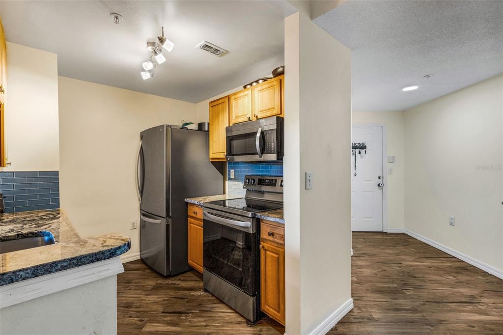 A kitchen with stainless steel appliances, wood cabinets, and blue tile backsplashes — 5601 BENTGRASS DRIVE UNIT 10-202, SARASOTA, FL