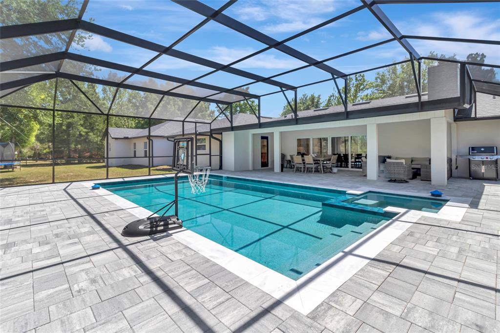 A screened-in pool area with a basketball hoop, patio furniture, and light-colored stone pavers — 12305 HOWEY CROSS ROAD, CLERMONT, FL