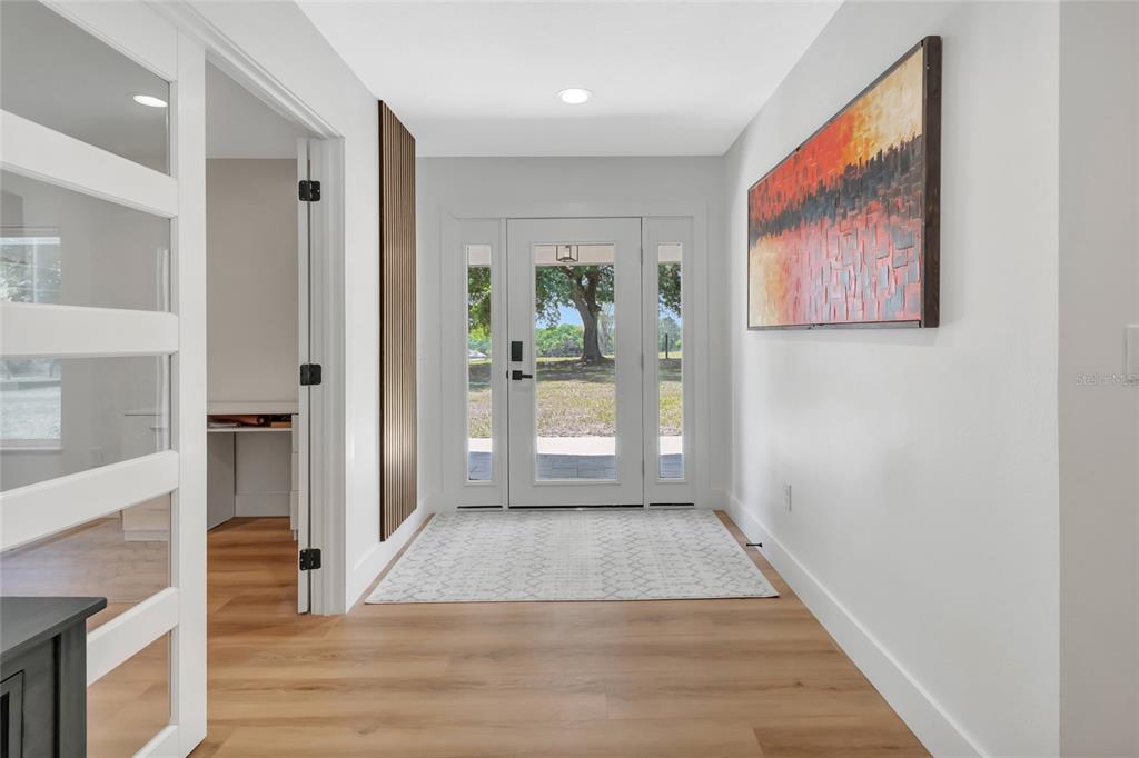A bright entryway features light wood flooring, a white front door, and abstract wall art — 12305 HOWEY CROSS ROAD, CLERMONT, FL