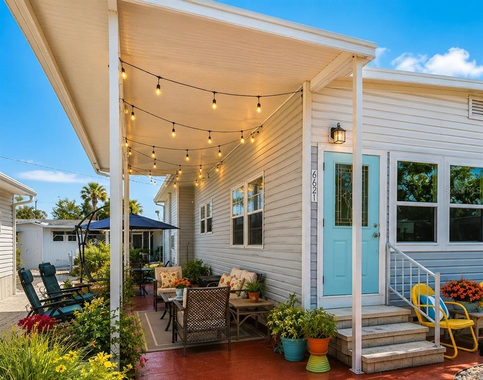 A covered patio features string lights, outdoor furniture, and a light blue front door — 6621 MARINA DRIVE, BRADENTON, FL