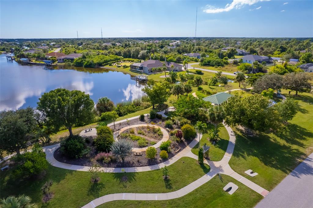 An aerial view shows a landscaped garden with walking paths beside a lake and houses — 10098 ARMY CIRCLE, PORT CHARLOTTE, FL