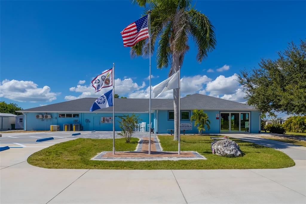 A light blue building with a gray roof stands behind three flagpoles and palm trees — 10098 ARMY CIRCLE, PORT CHARLOTTE, FL