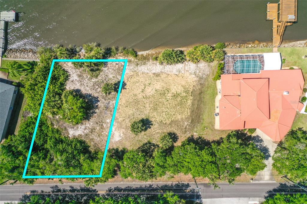 An aerial view shows a vacant waterfront lot outlined in blue next to a house — 3680 JOHN ANDERSON DR, ORMOND BEACH, FL