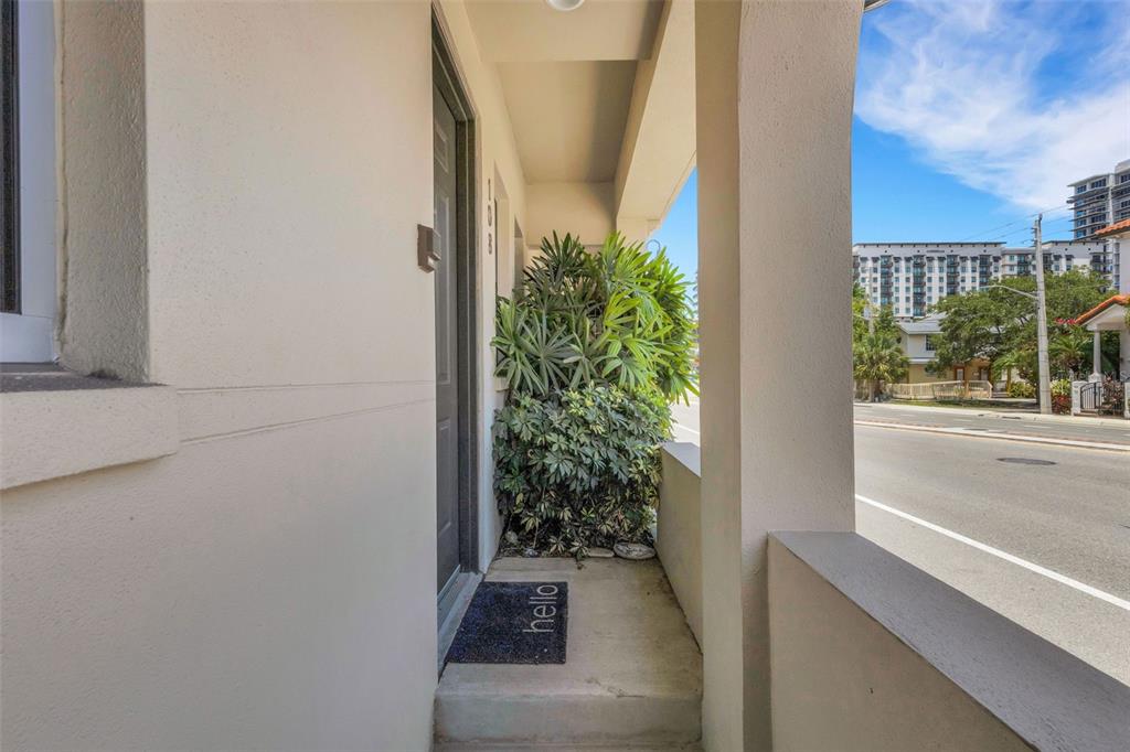 A covered porch entrance features a dark door, a hello mat, and a large potted plant — 235 COCOANUT AVENUE UNIT 108B, SARASOTA, FL