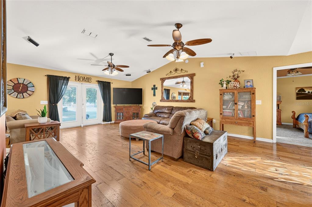 A living room features hardwood floors, vaulted ceilings with two fans, and a brown sofa — 14115 NE 47TH AVENUE, ANTHONY, FL