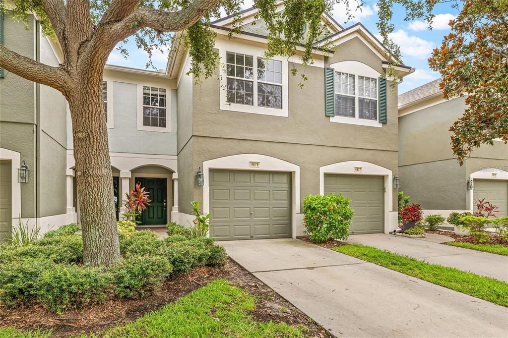 A two-story townhouse exterior with two garage doors, green shutters, and a large front tree — 4879 POND RIDGE DRIVE, RIVERVIEW, FL