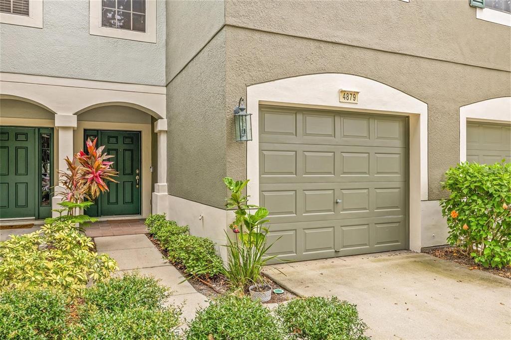 The exterior of a townhouse features a green garage door, a front entrance, and landscaping — 4879 POND RIDGE DRIVE, RIVERVIEW, FL