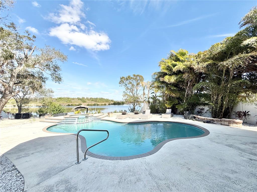 A swimming pool with a spa overlooks a lake surrounded by trees and lounge chairs — 6710 MYRNA DRIVE, TAMPA, FL