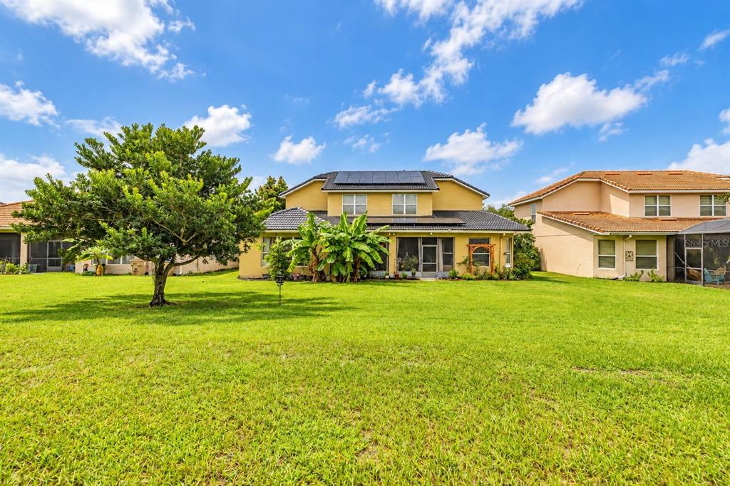 The rear exterior of a two-story house with solar panels and a large grassy yard — 3713 EAGLE ISLE CIRCLE, KISSIMMEE, FL
