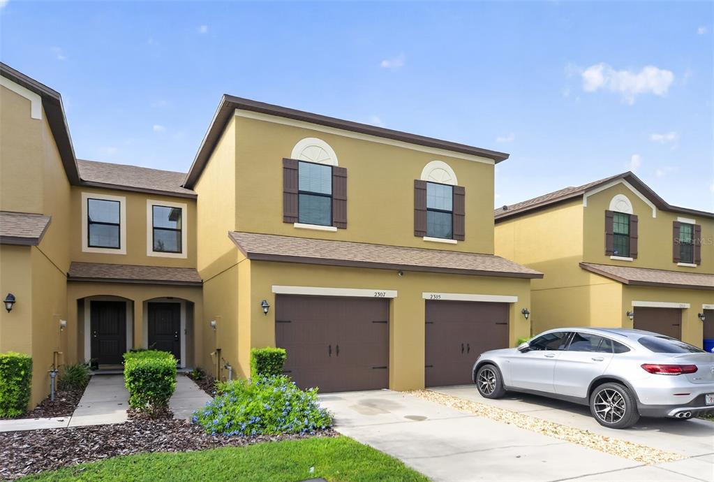 A two-story townhouse exterior features tan stucco walls, brown garage doors, and a silver sedan — 2307 ALOHA BAY COURT, OCOEE, FL