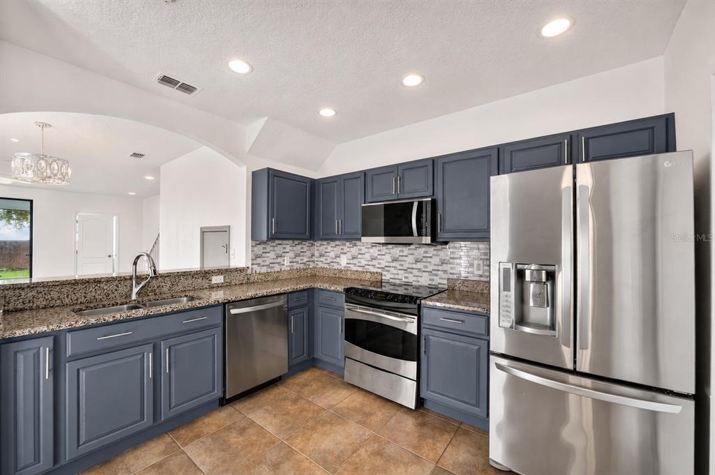 A kitchen features blue cabinets, granite countertops, stainless steel appliances, and a tiled floor — 2307 ALOHA BAY COURT, OCOEE, FL