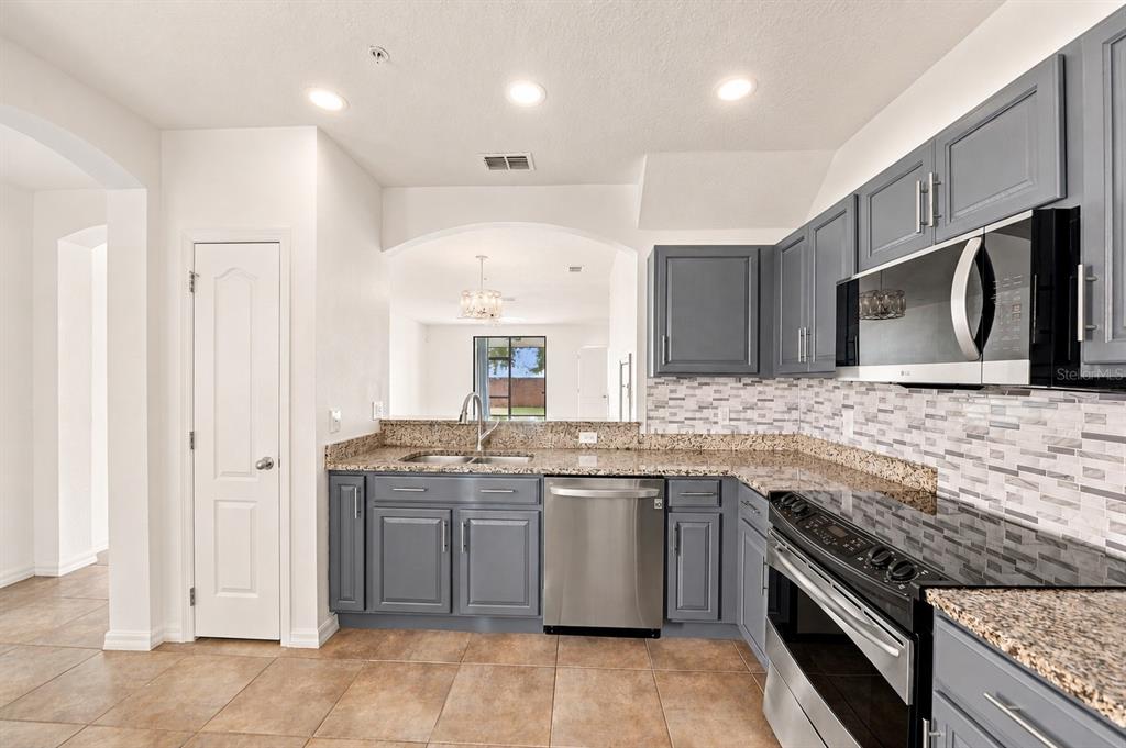 A kitchen with gray cabinets, granite countertops, stainless steel appliances, and a tiled backsplash — 2307 ALOHA BAY COURT, OCOEE, FL