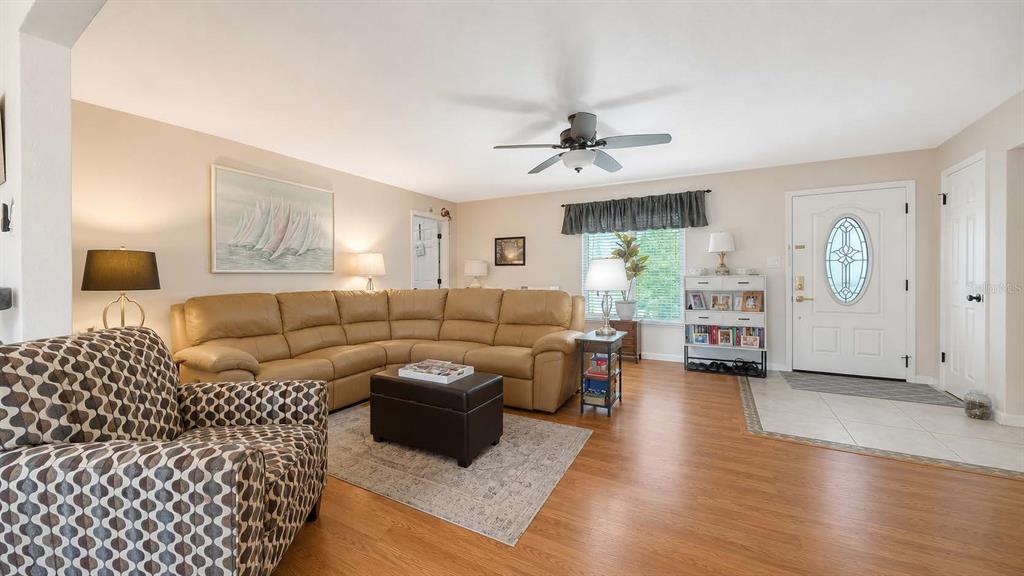 A living room features a tan sectional sofa, a patterned armchair, and a white front door — 6926 ANTIGUA PLACE, SARASOTA, FL