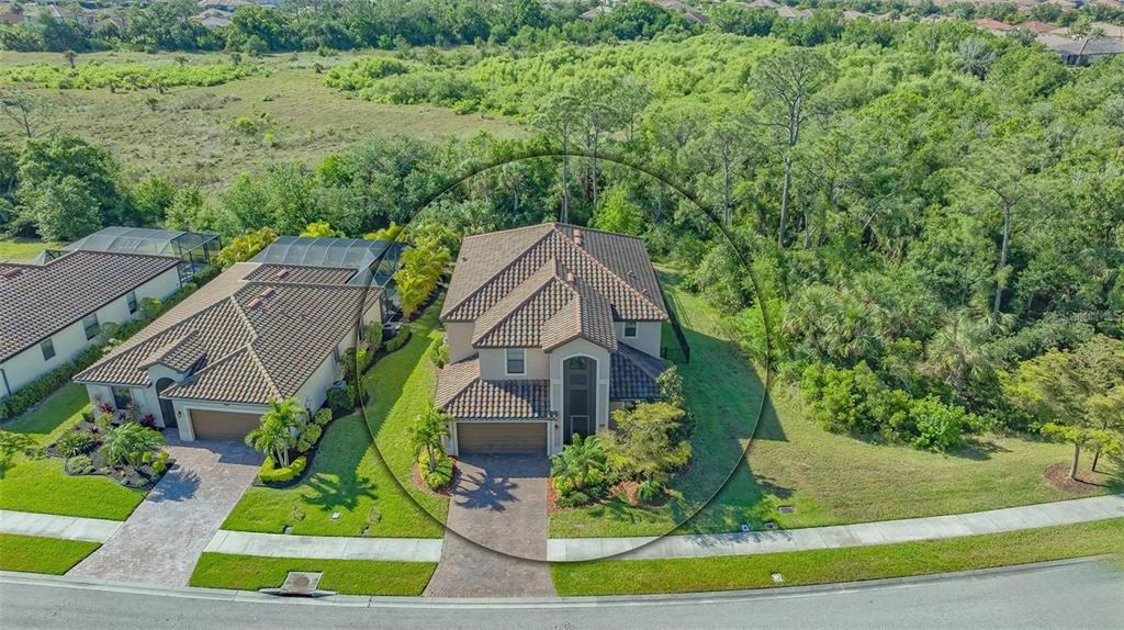 An aerial view shows a two-story house with a tiled roof surrounded by lush greenery — 12801 CINQUETERRE DRIVE, VENICE, FL