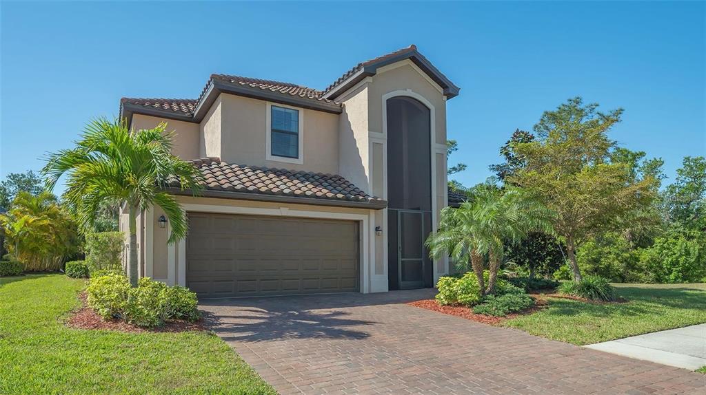 A two-story house with a tan stucco exterior, a brown garage door, and a screened entryway — 12801 CINQUETERRE DRIVE, VENICE, FL