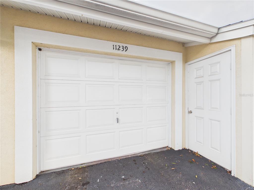 A white garage door and a matching side entry door are set in a stucco wall — 11239 CEDAR HOLLOW LANE, TAMPA, FL