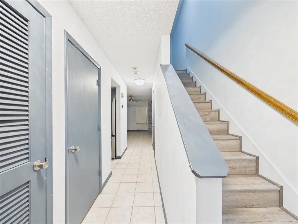 A hallway with tiled floors, a staircase with wood-look treads, and several gray doors — 11239 CEDAR HOLLOW LANE, TAMPA, FL